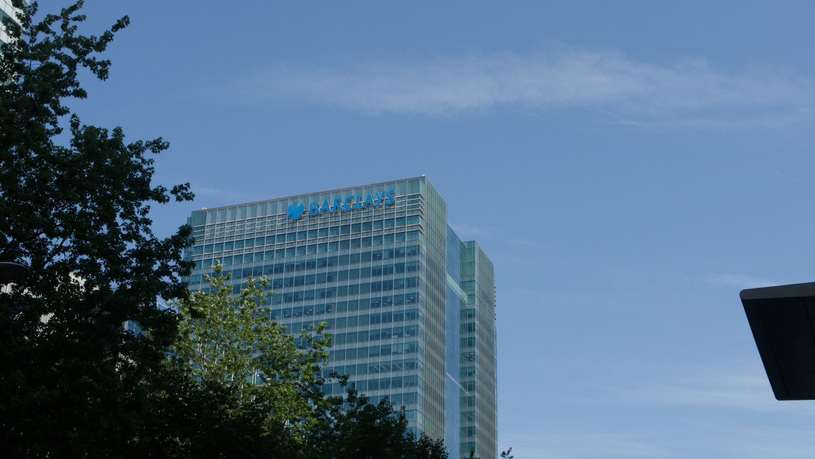 Barclays building under a clear blue sky with green trees