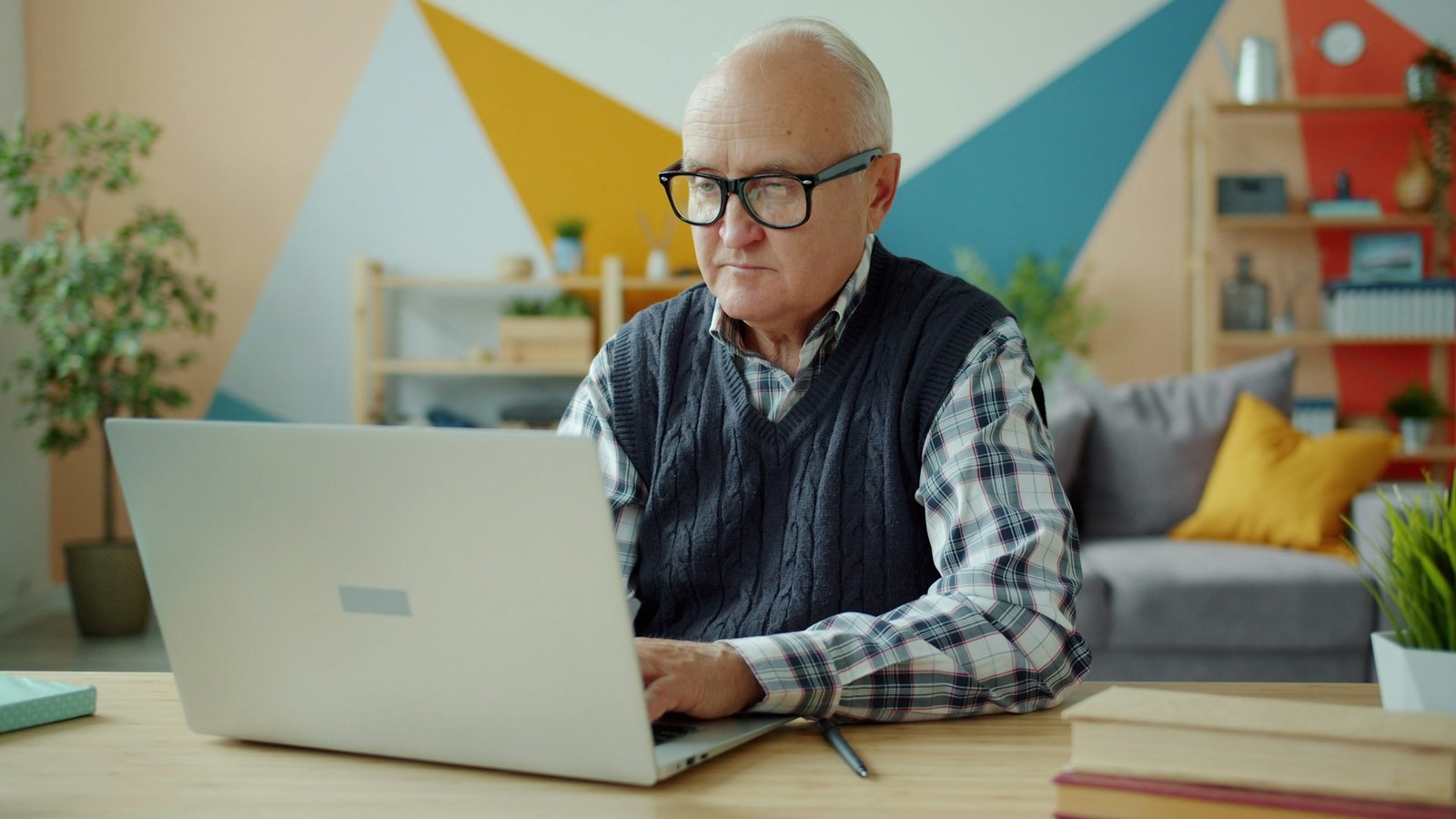 Elderly man wearing glasses using a laptop at home